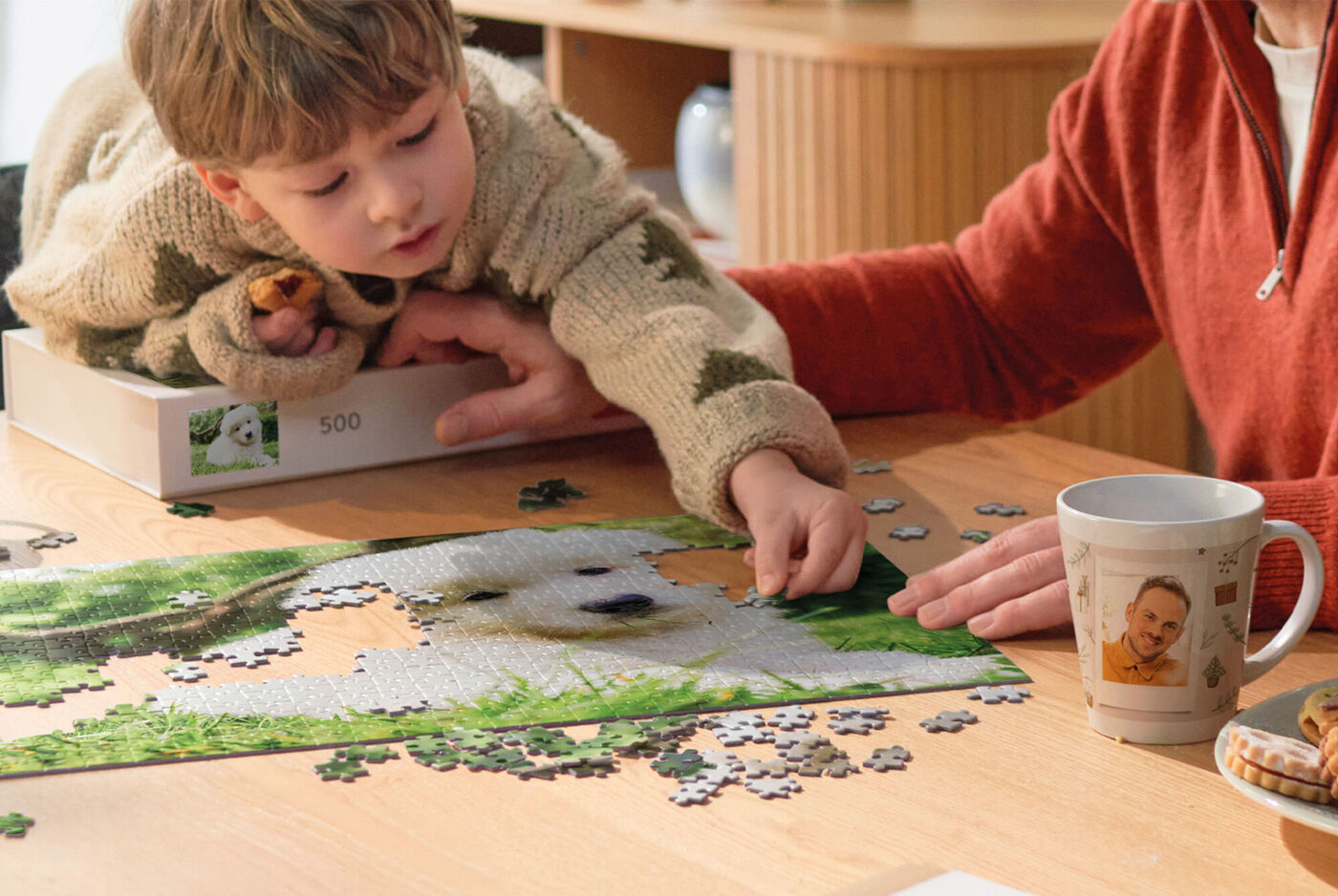 Ein Kind und eine Erwachsene Person sitzen am Tisch und legen gemeinsam ein Fotopuzzle zusammen.