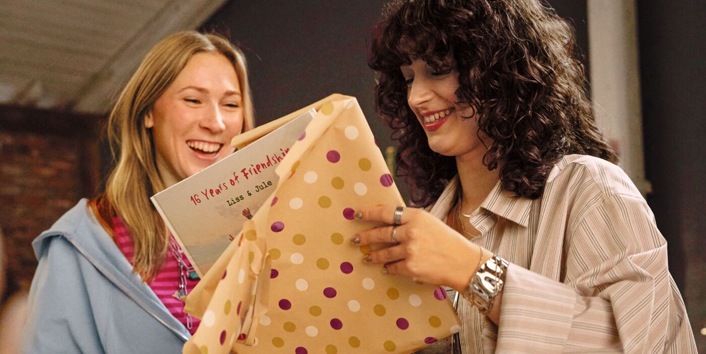 Zwei Freundinnen freuen sich über ein Geschenk mit einem CEWE Fotobuch zu 16 Jahren Freundschaft.
