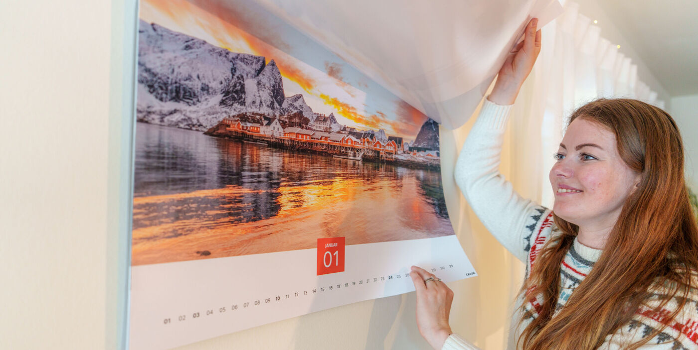 Person blättert in einem CEWE Wandkalender XXL mit einem Bild von einer Fjordlandschaft