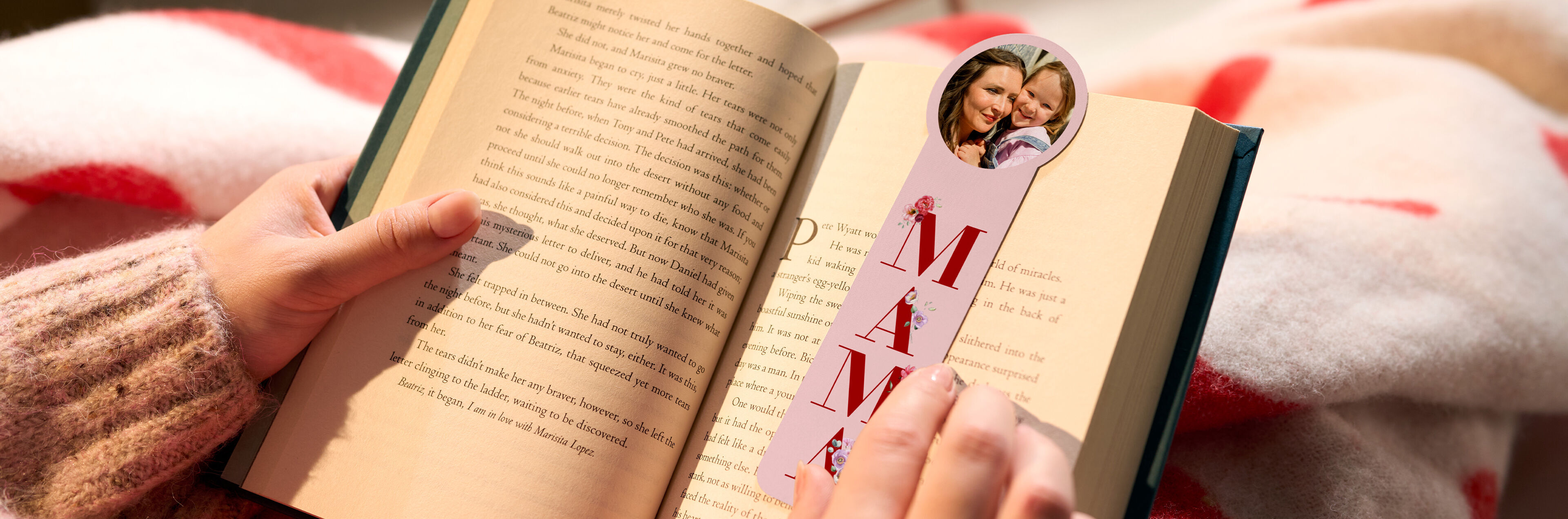 Hand hält ein Buch und ein Foto-Lesezeichen mit einem Foto von Mutter und Kind und dem Schriftzug "MAMA".