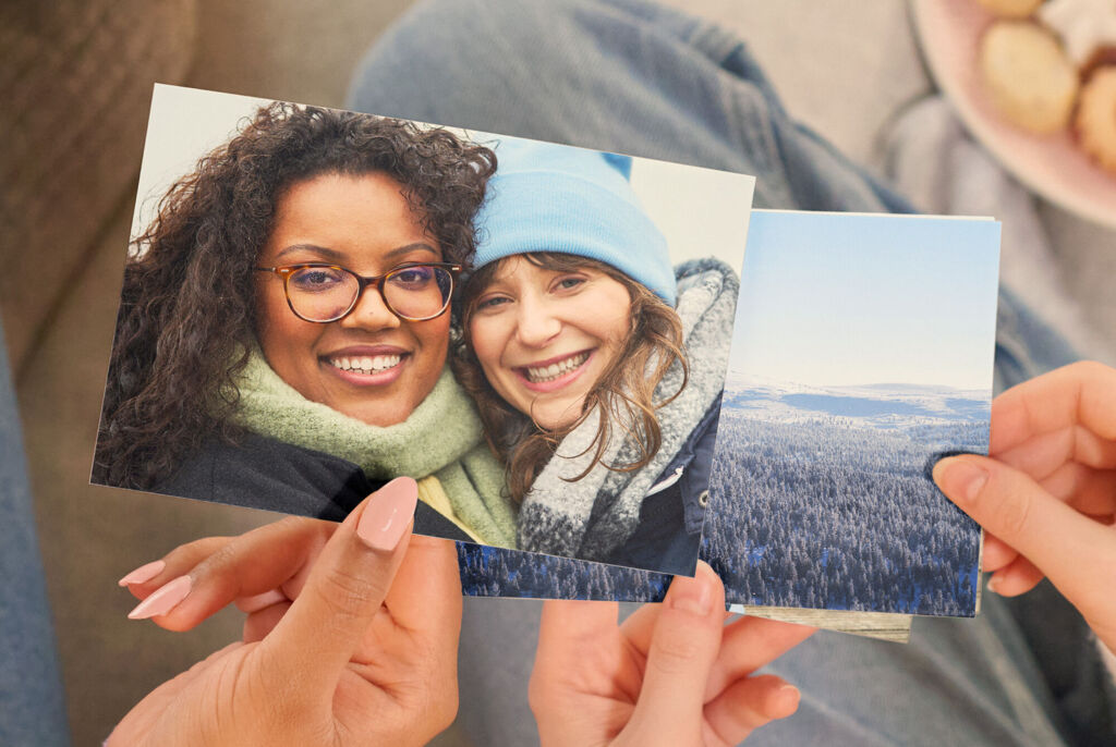 Zwei lächelnde Freundinnen halten Fotos mit winterlichen Bildern.