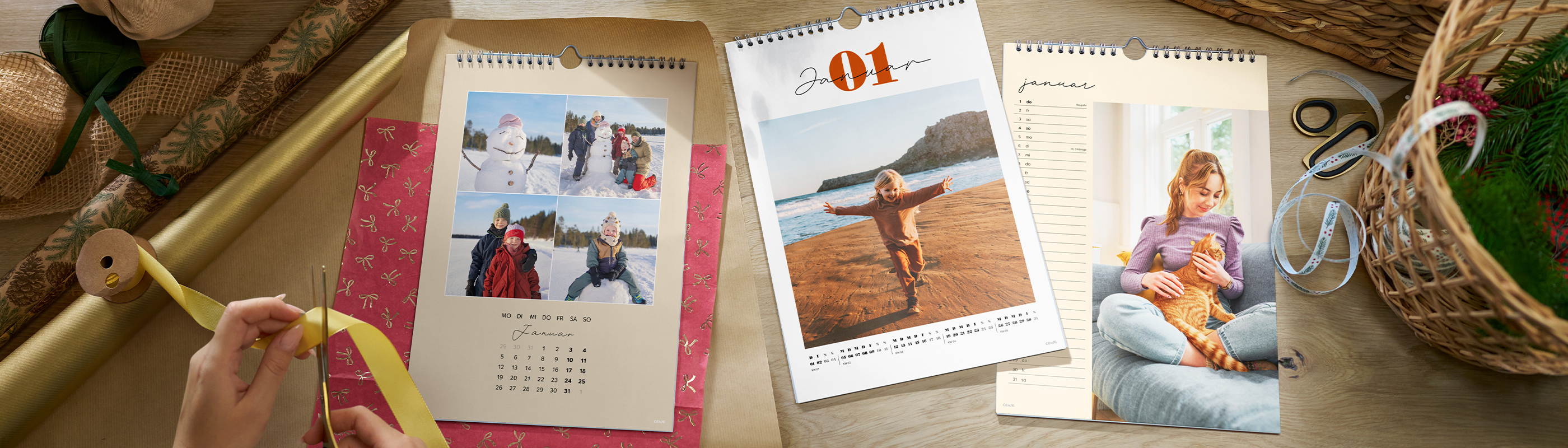 Mehrere CEWE Fotokalender mit persönlichen Fotos liegen neben Geschenkband und Bastelmaterial
