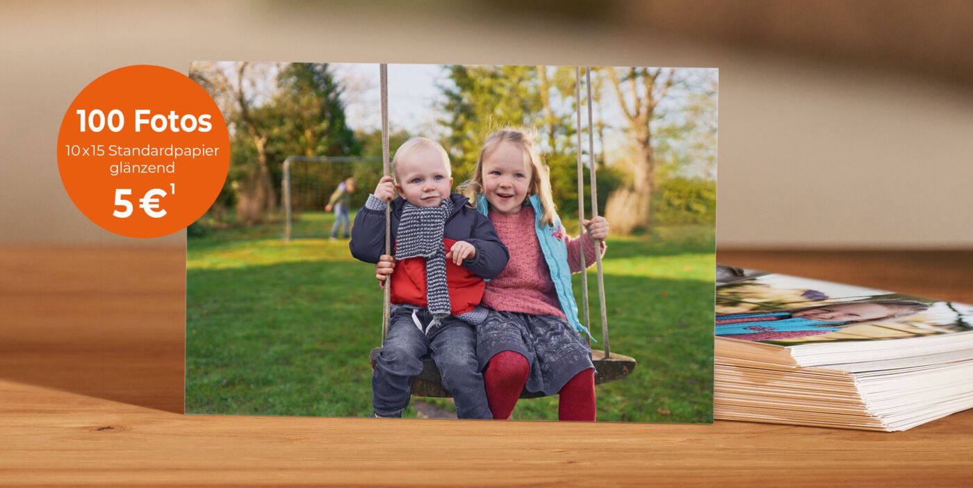 Hände halten mehrere glänzende Fotoabzüge; auf dem obersten Foto sieht man zwei Kinder auf einer Schaukel.
