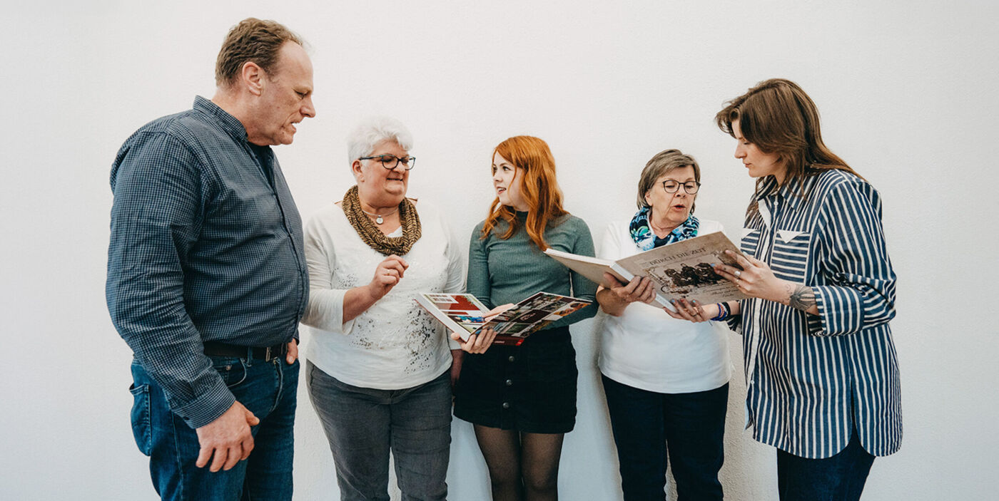 Fünf Personen betrachten und besprechen gemeinsam mehrere Fotobücher von CEWE.