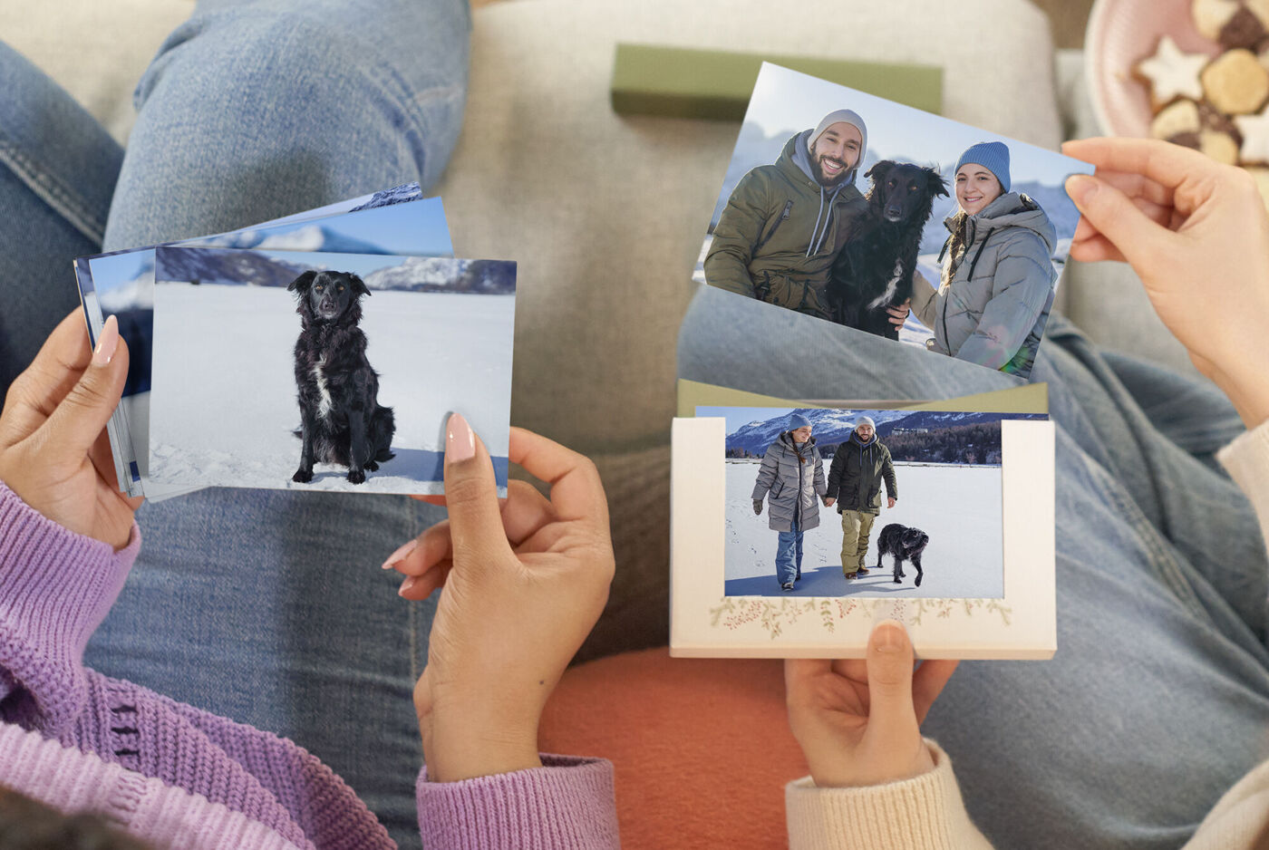 Zwei Personen halten Fotokarten mit Bildern eines Hundes und von sich im Schnee.