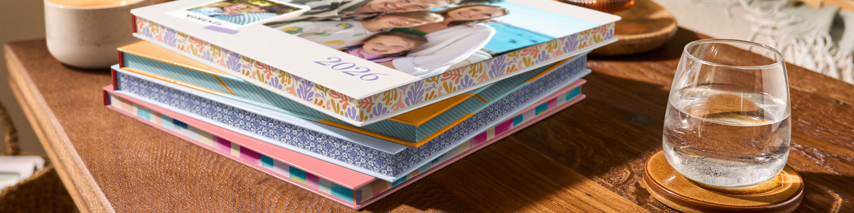 Mehrere CEWE FOTOBÜCHER mit buntem Farbschnitt an den Seitenkanten liegen auf einem Holztisch
