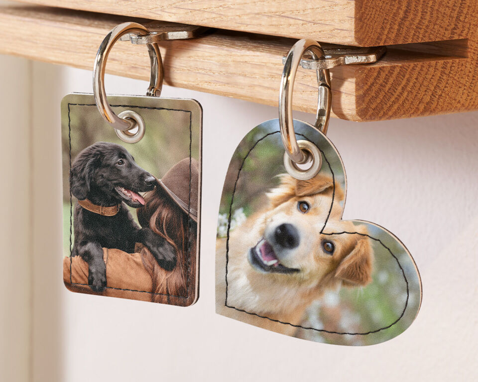 Zwei personalisierte Schlüsselanhänger mit Fotos von Hunden hängen an einem hölzernen Schlüsselbrett.