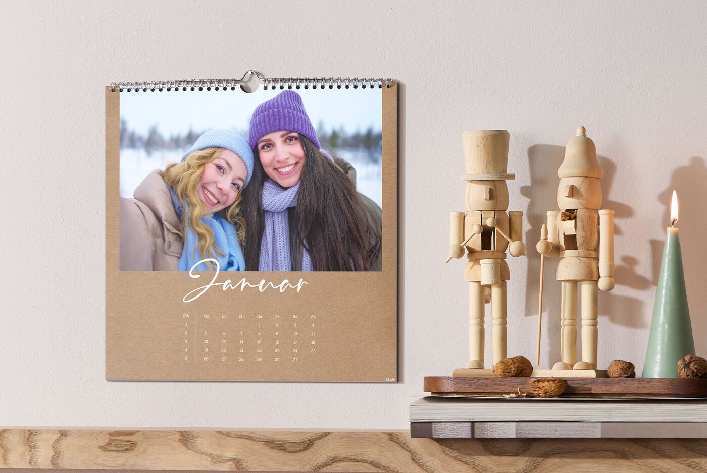 Zwei Personen mit Wintermützen auf CEWE Fotokalender, daneben Holz-Nussknacker, Kerze und Walnüsse