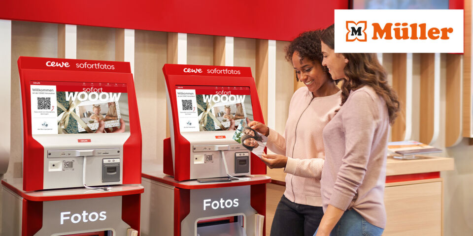 Zwei Personen nutzen rote CEWE Sofortfoto-Automaten in einer Müller-Filiale.