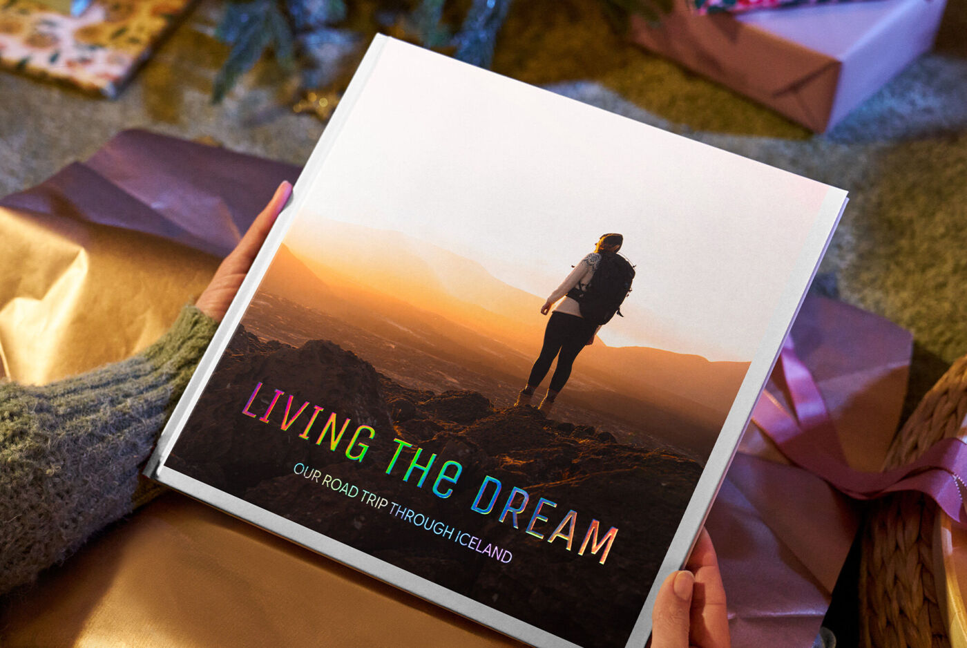 Eine Person hält ein CEWE FOTOBUCH mit Landschaftsbild und dem Titel „Living the Dream“.