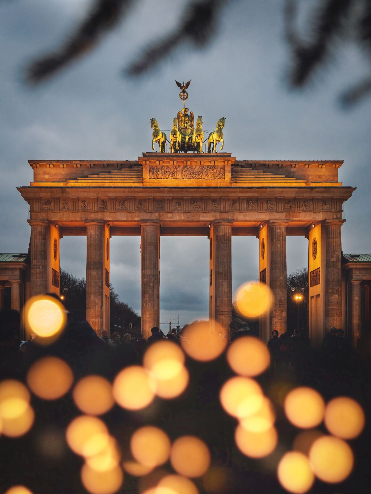 Brandenburger Tor am Abend. Im Vordergrund warme Lichtpunkte einer Lichterkette.