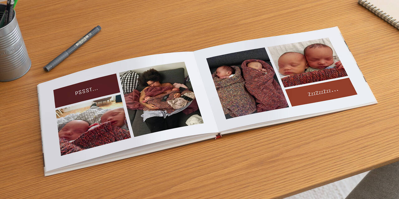 Ein aufgeschlagenes CEWE FOTOBUCH liegt auf einem Tisch. Auf beiden Seiten sieht man neugeborene Zwillinge beim Schlafen mit den Texten "Psst" und "Zzz" in verschiedenen Schriften.